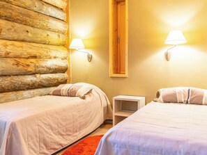A room with two beds, wooden log wall, and two wall-mounted lamps.