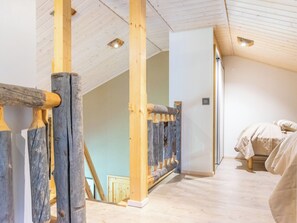 A room with wooden beams, a sloped ceiling, and a bed with a white cover.