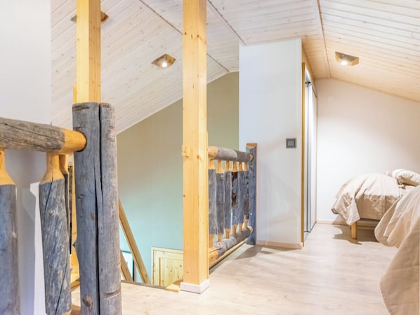 Een kamer met houten balken, een schuine plafond en een bed met een witte spreidek.