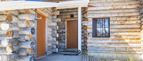 A log cabin with a wooden deck, two doors, and a window.