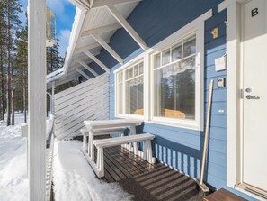 Una terraza de madera con un banco y una puerta a un edificio con revestimiento azul y detalles blancos.