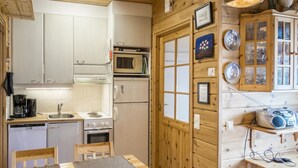 Une cuisine compacte comprenant un coin repas, des placards en bois, un four à micro-ondes, un réfrigérateur et une petite table avec des chaises.