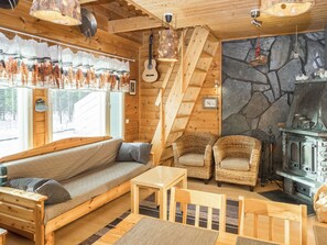 L’intérieur d’un chalet accueillant, avec un escalier en bois, un mur en pierre, une cheminée et un canapé agrémenté de coussins.