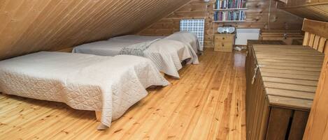 A cozy attic bedroom with wooden floors and sloped ceilings, featuring two beds and a bookshelf.