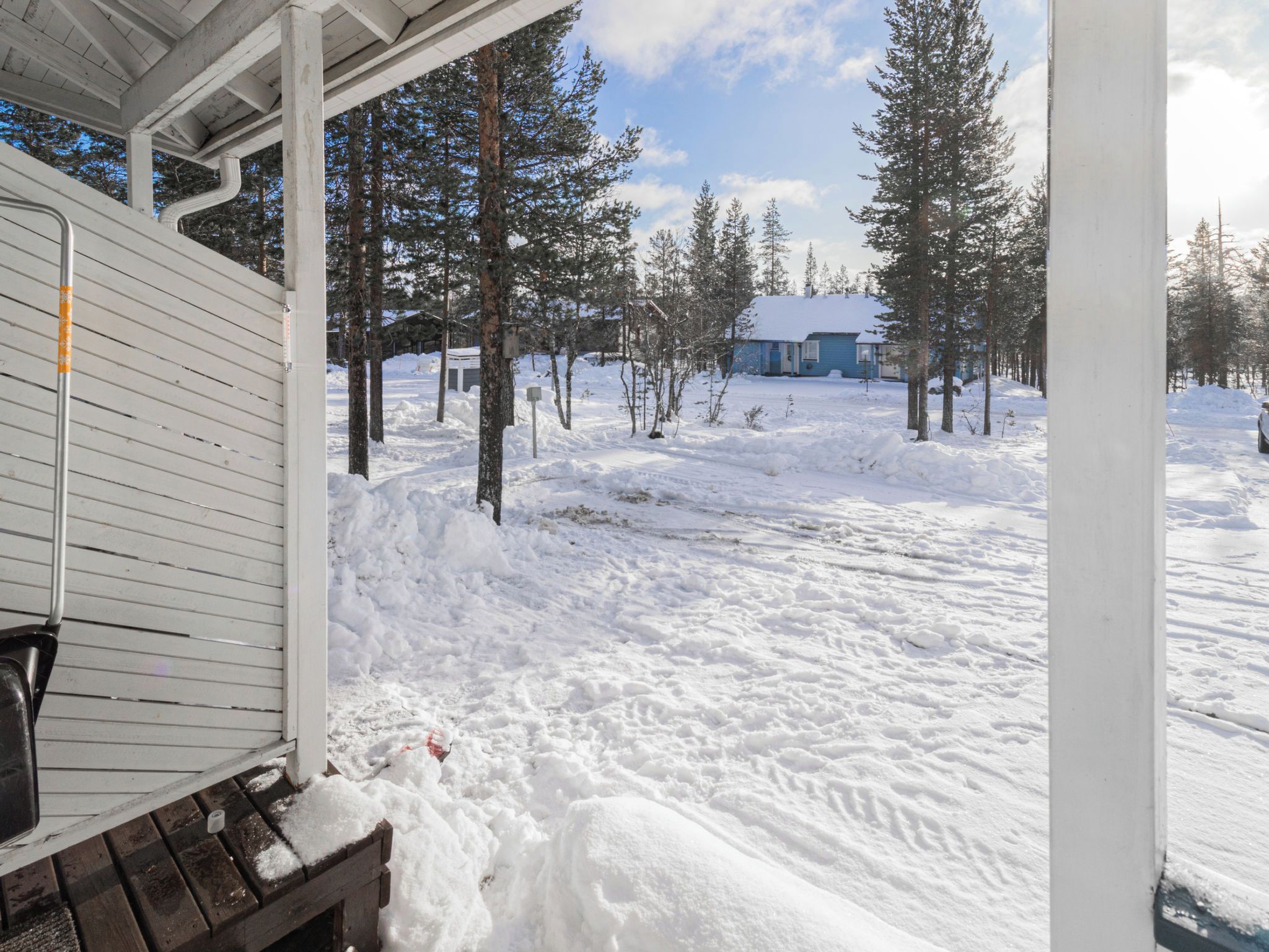 A snow-covered outdoor area with a wooden bench and a building in the background.