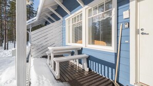 Une terrasse en bois avec un banc, une porte marquée du signe « B » et une fenêtre avec des stores.