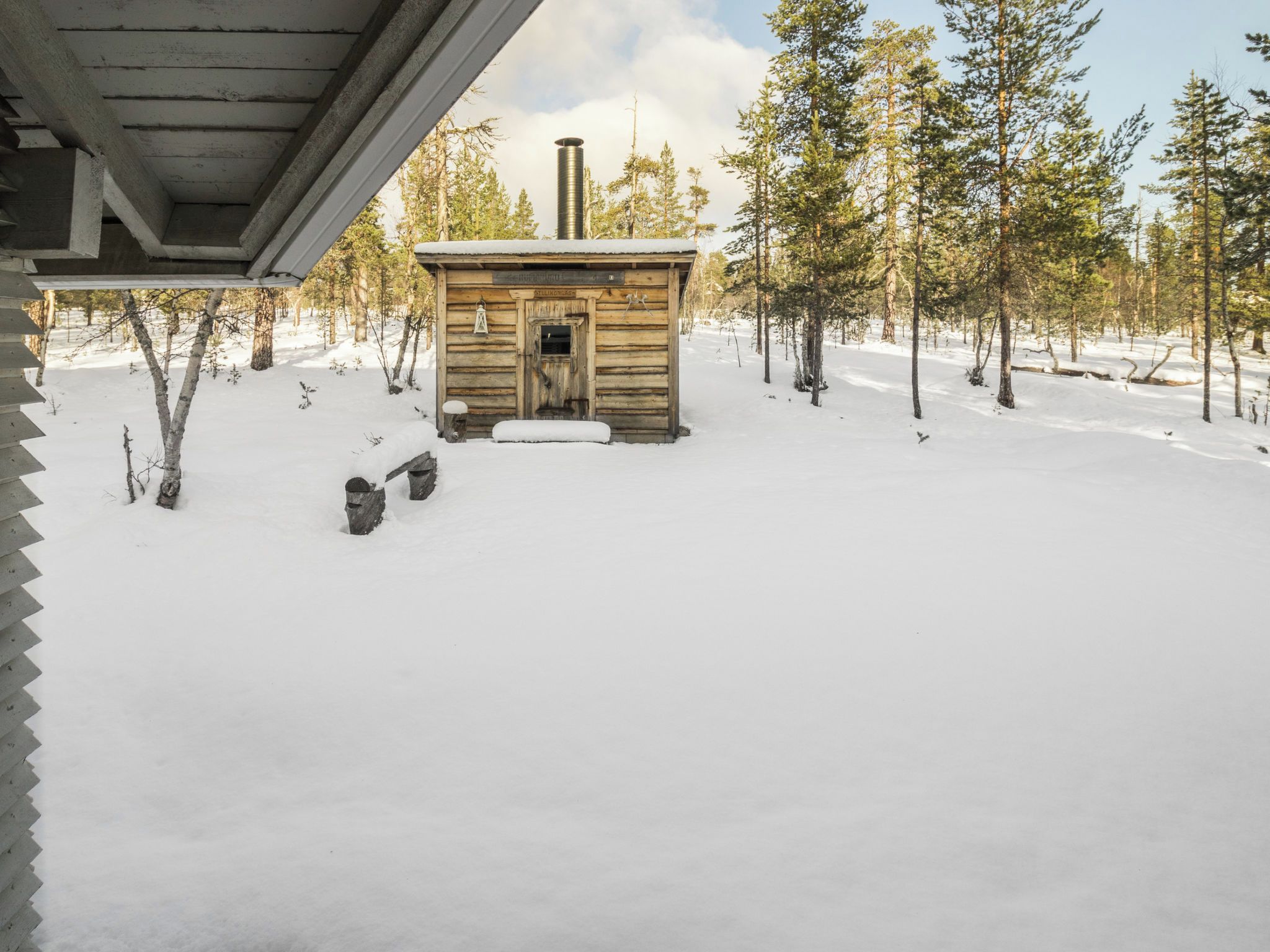 Une cabane en bois avec une cheminée, entourée d’un paysage enneigé et d’arbres.