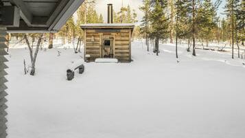 Une cabane en bois avec une cheminée, entourée d’un paysage enneigé et d’arbres.
