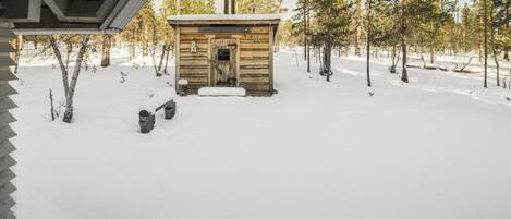 Una cabaña de madera con chimenea, rodeada de nieve y árboles.