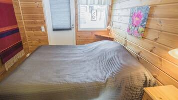 Une pièce en bois avec un lit, une porte, une fenêtre et une lampe fixée au mur.