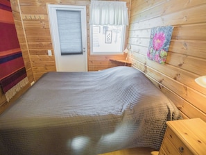 Une pièce en bois avec un lit, une porte, une fenêtre et une lampe fixée au mur.