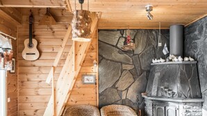 L’intérieur chaleureux d’un chalet avec un escalier en bois, un mur en pierre, une cheminée, des fauteuils en osier et une guitare.