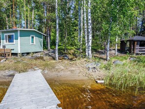 A cabin with a dock extending into a clear stream, surrounded by a forest.