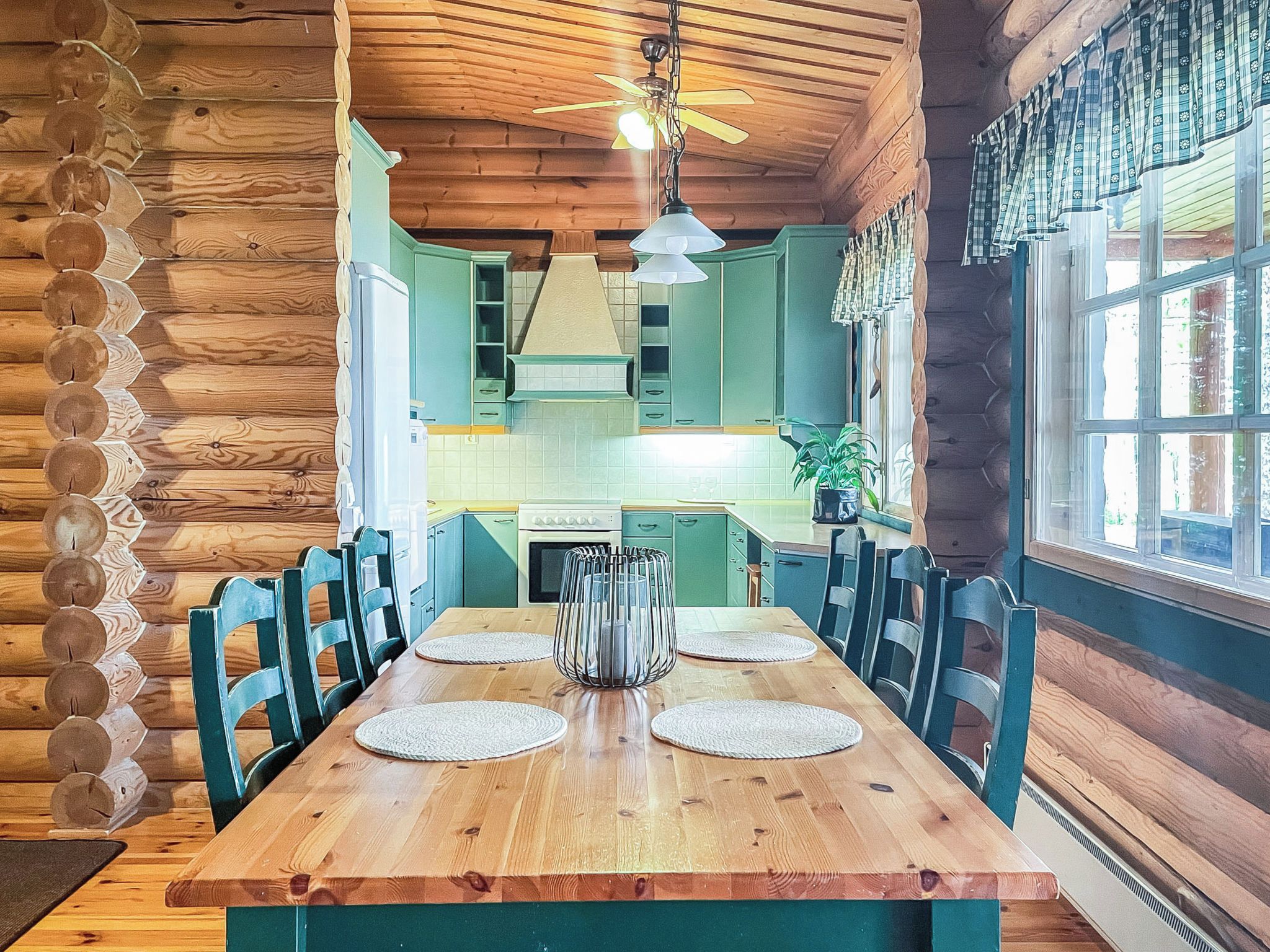 Una mesa de comedor de madera con sillas, un ventilador de techo y una ventana con cortinas.