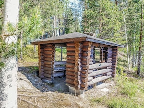 A rustic wooden cabin with a sloped roof, surrounded by a forest.