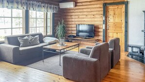 Un saló tranquil amb sostre de fusta, un sofà, una taula de centre, un televisor i una finestra gran amb cortines.