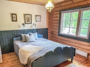 A wooden-paneled bedroom with a bed, two wall-mounted lamps, and a window with a view of greenery.