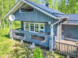 A wooden cabin with a deck, large windows, and a satellite dish.