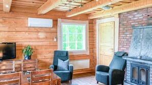 L’intérieur chaleureux d’un chalet avec un décor en bois, une cheminée en pierre, un coin repas avec des chaises et un téléviseur.
