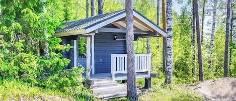 En liten stuga med en veranda, omgiven av träd och grönska.