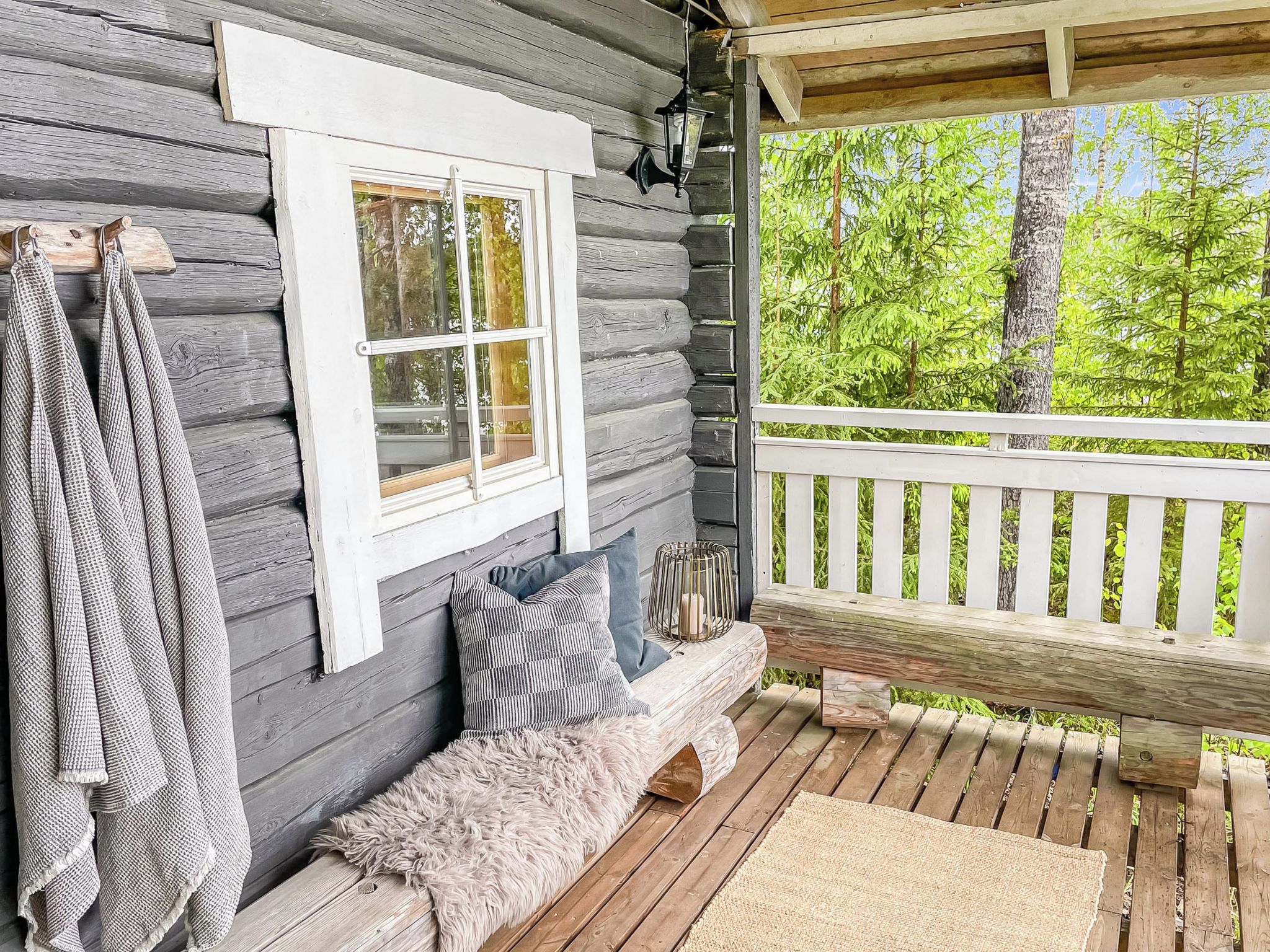 A wooden cabin with a porch, a bench with cushions, and a hanging towel.
