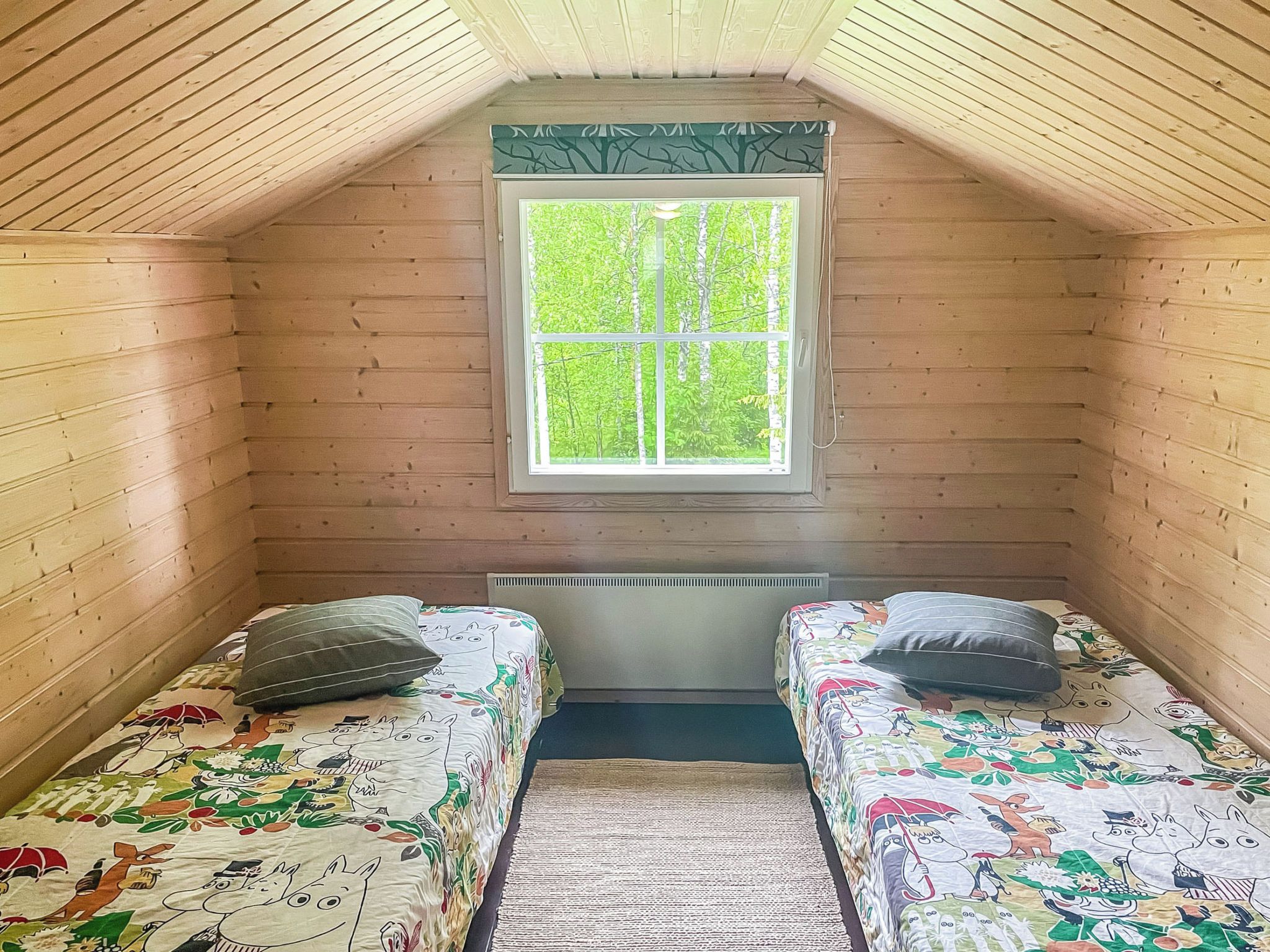A small, cozy room with two single beds, a window with a view of greenery, and a radiator under the window.