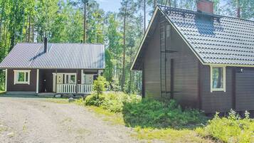 Mökki, jossa on kuisti ja savupiippu, ja sen ympärillä on tiheää metsää.