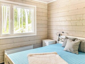 Un dormitorio con cama, mesita de noche, lámpara y ventana con vistas a árboles.