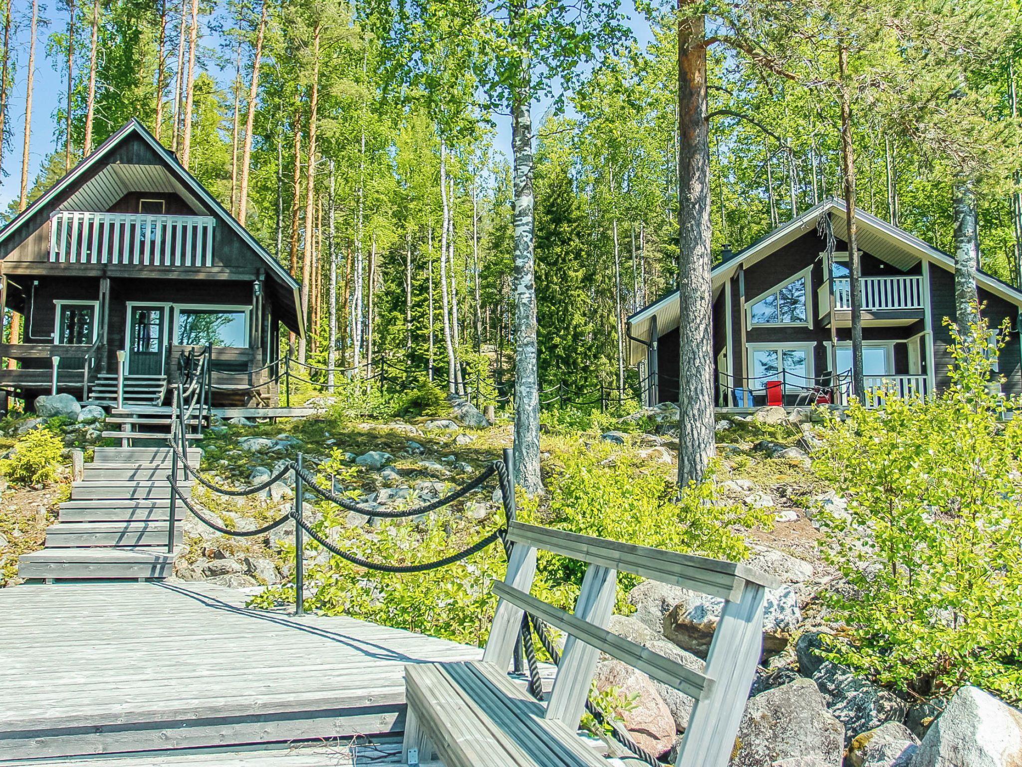 Eine Holzhütte mit einer Terrasse, die zum Eingang führt, umgeben von einem Wald.
