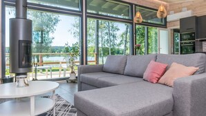 Una sala de estar moderna con un sofá gris, una mesa redonda blanca y un gran ventanal con vistas a un lago.