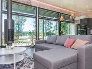 Een moderne woonkamer met een grijze bank, een ronde witte tafel en een groot raam met uitzicht op bomen en een meer.