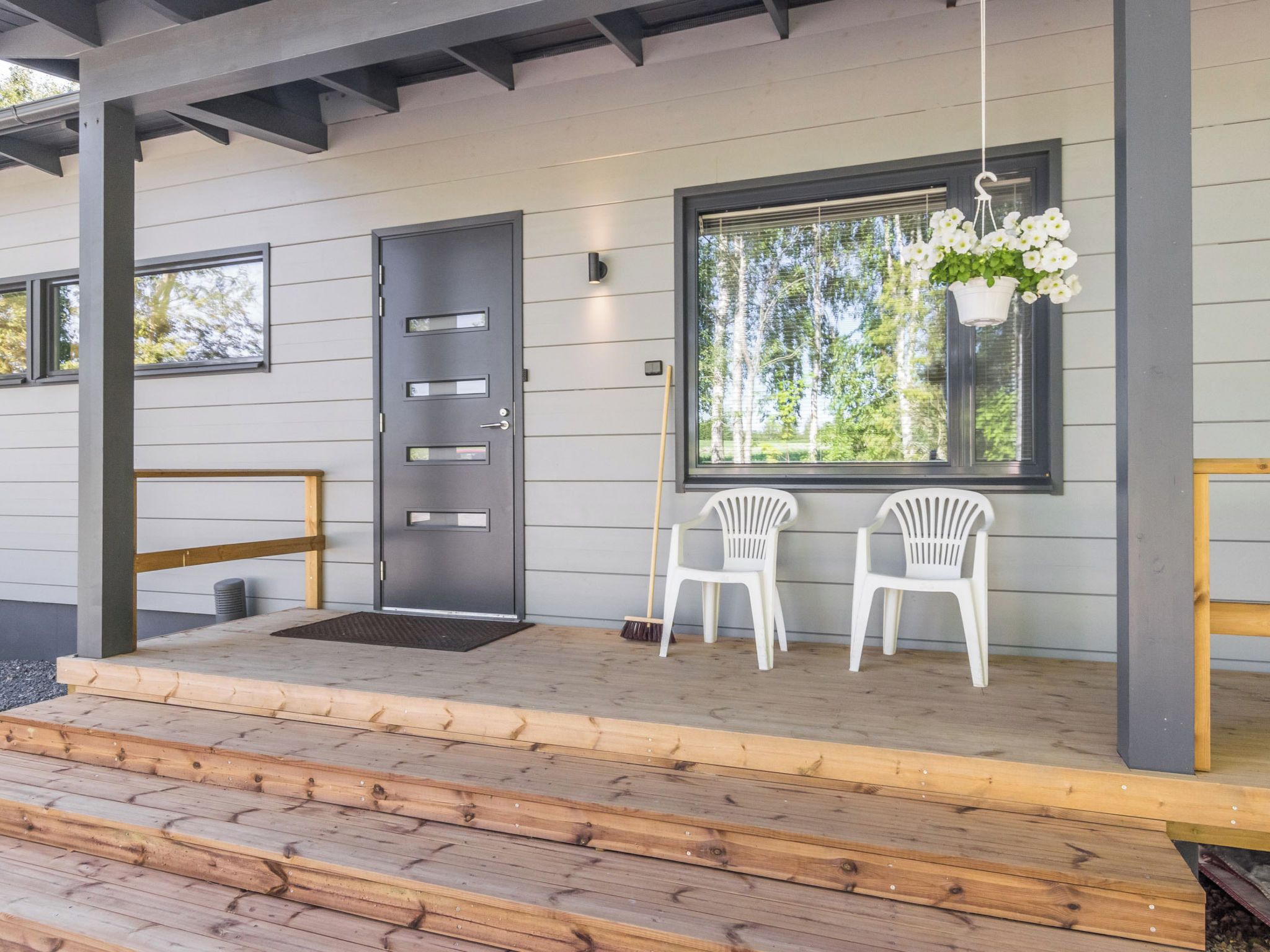 A wooden deck with a gray door, two white plastic chairs, and a hanging flower pot.