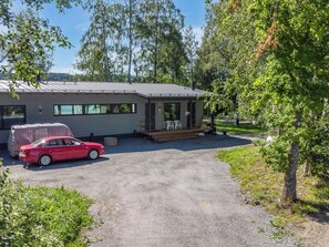 Un bâtiment d’un seul étage, doté d’un porche couvert, d’une allée en gravier et d’une voiture rouge garée devant.