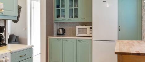 A kitchen with light green cabinets, a white refrigerator, a microwave, and a coffee maker.