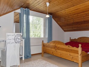 A bedroom with a sloped ceiling, a wooden bed, a white desk, and a window with blue curtains.