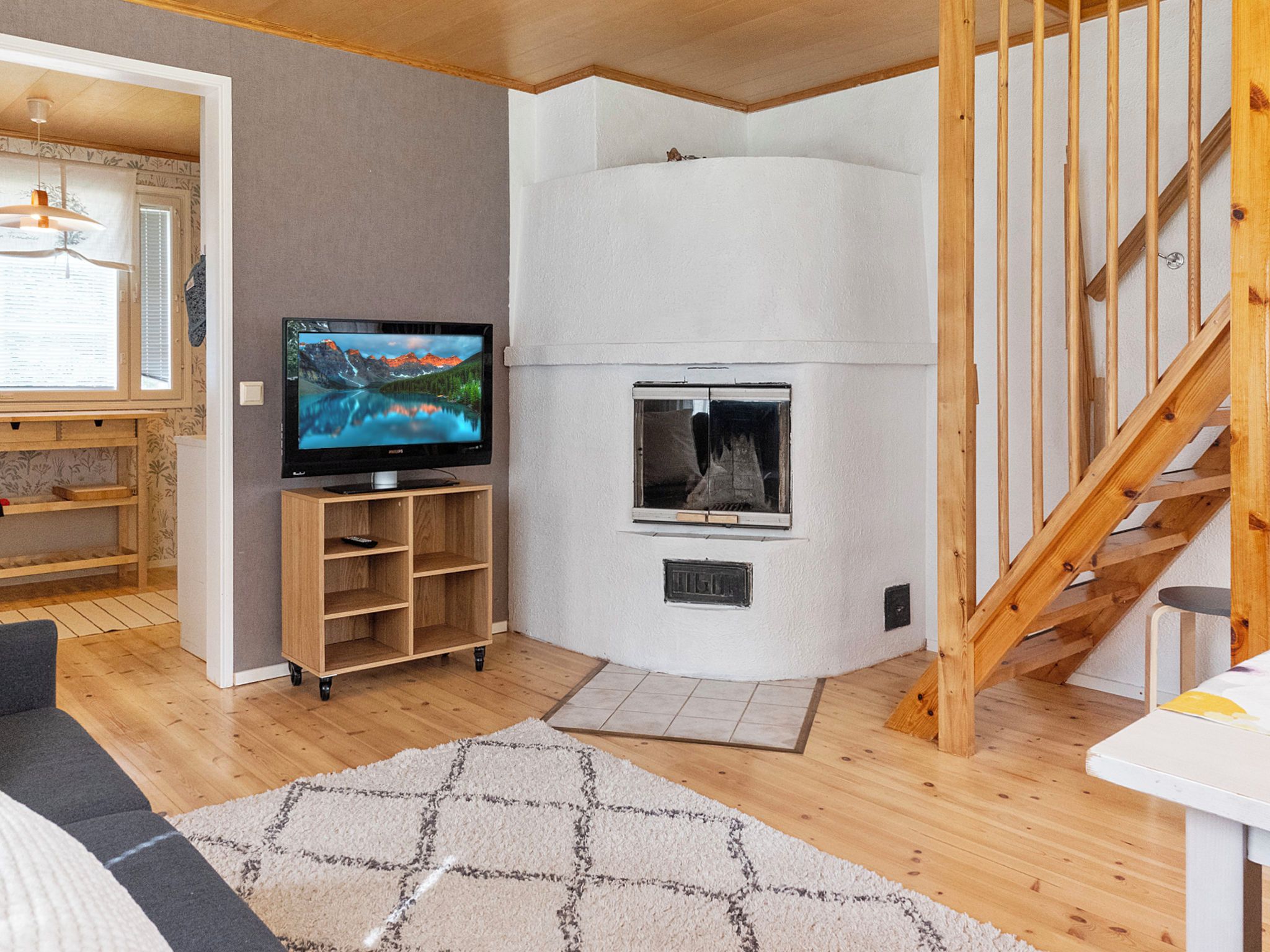 Ein Wohnzimmer mit Fernseher, Kamin, einer Holztreppe und Blick ins Freie.
