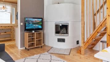 Ein Wohnzimmer mit Fernseher, Kamin, einer Holztreppe und Blick ins Freie.
