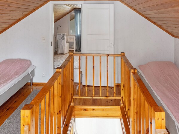 A dormitory room with two single beds, a wooden staircase, and a white door leading to another room.