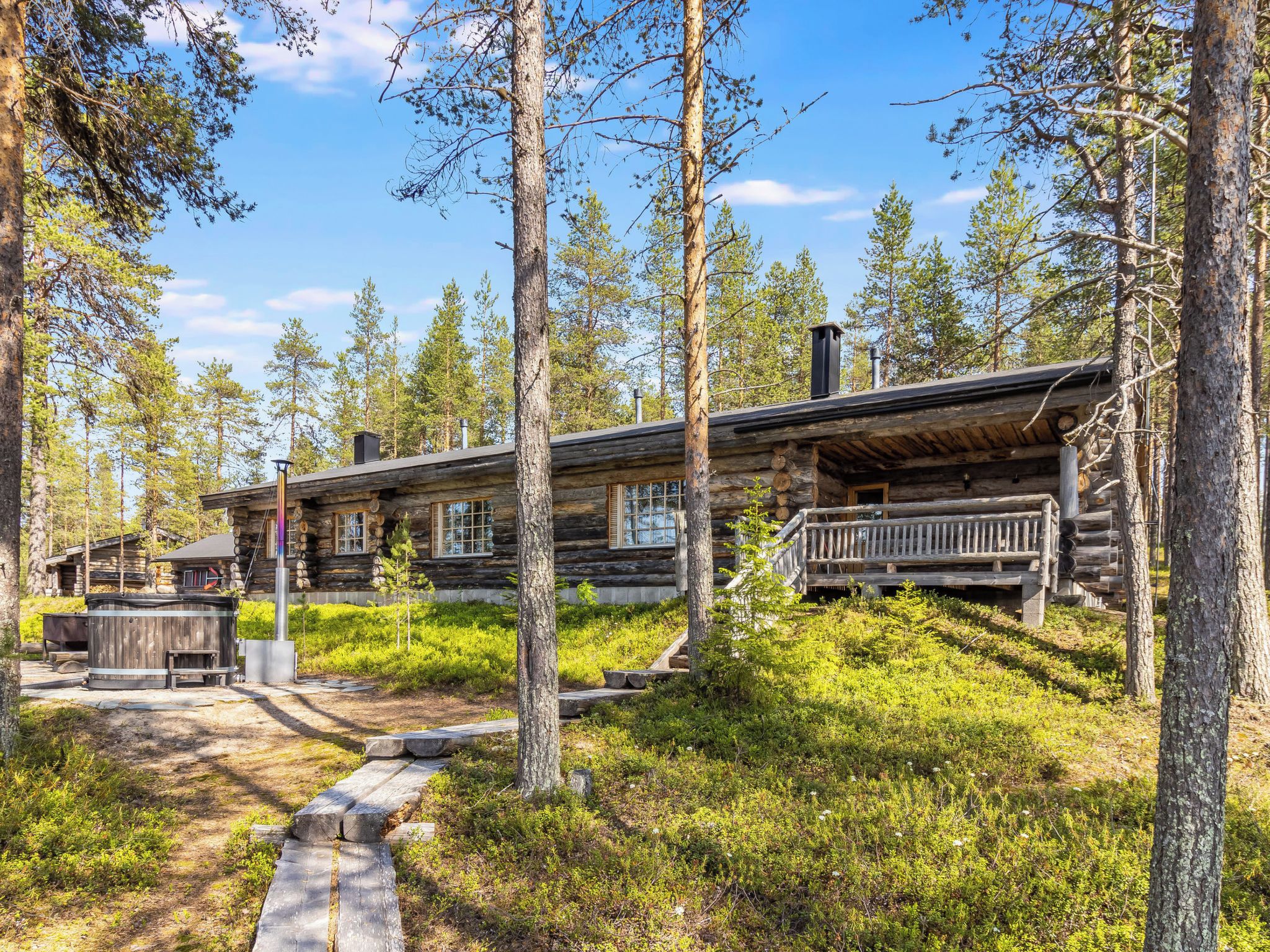 A log cabin with a deck, surrounded by trees and a clear sky.