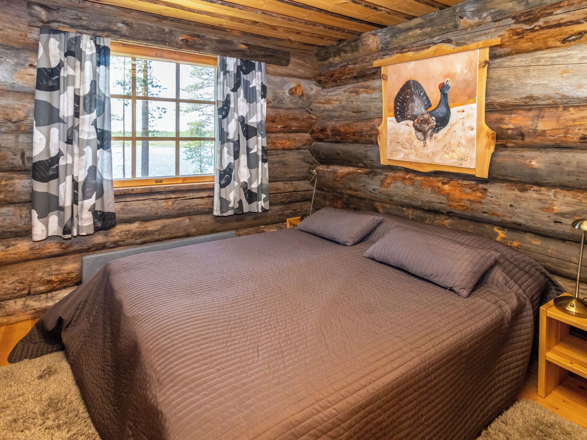 A log cabin bedroom with a bed, curtains, and a painting of a bird.