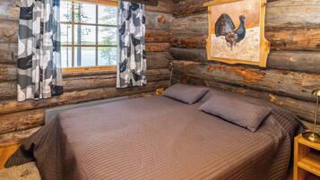 A log cabin bedroom with a bed, curtains, and a painting of a bird.