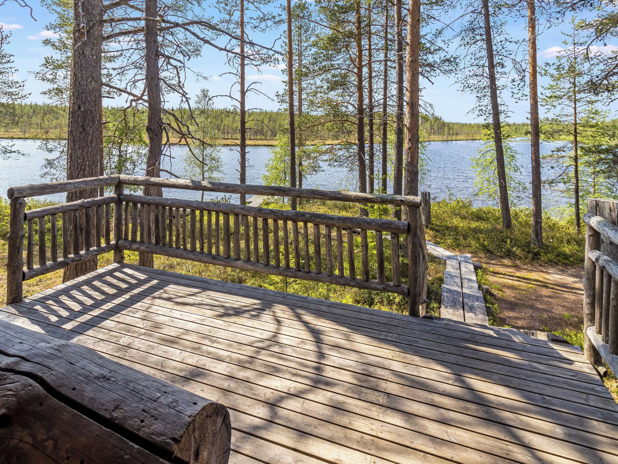 Eine Holzterrasse mit einer Bank, die auf einen See mit umliegenden Bäumen blickt.