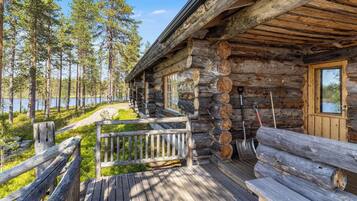 A log cabin with a wooden deck, a bench, and a view of a lake surrounded by trees.