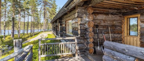 A log cabin with a wooden deck, a bench, and a view of a lake surrounded by trees.