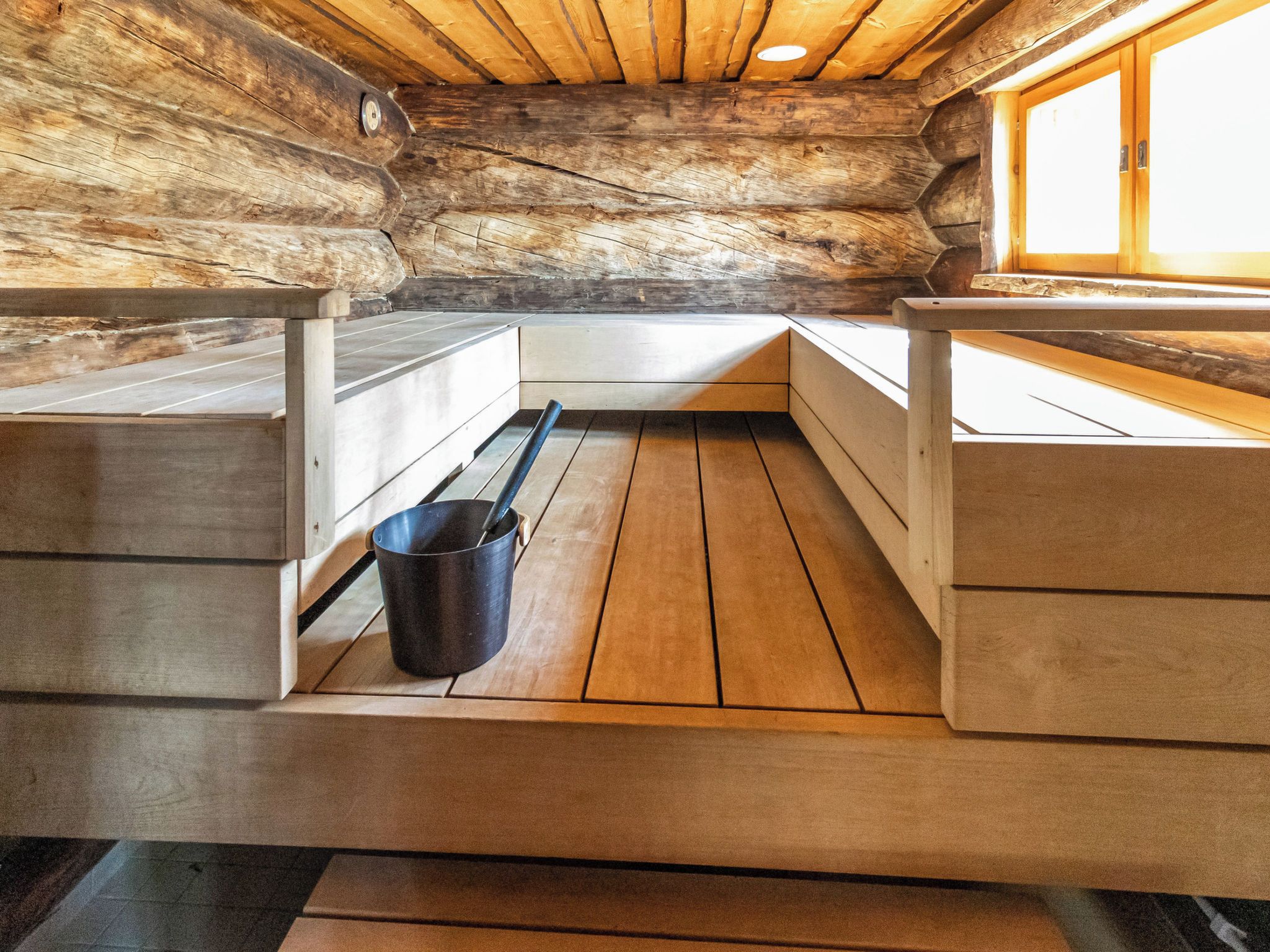 Interior de madera con un banco, un cubo y una ventana.