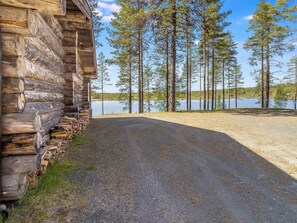 A log cabin with a gravel driveway leading to a lake surrounded by tall pine trees. - Villihanhi by Interhome (Kuusamo)