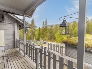 A wooden deck with a white picket fence, two lanterns, and a view of a forested area.
