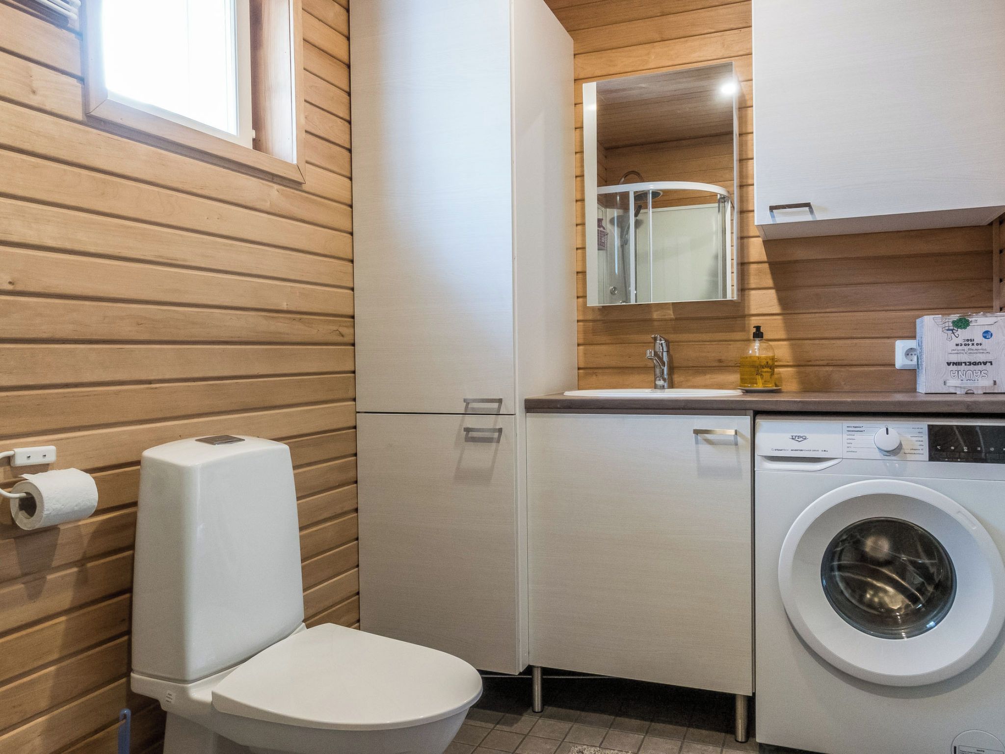 Un baño pequeño con inodoro, lavadora y espejo sobre el lavabo.