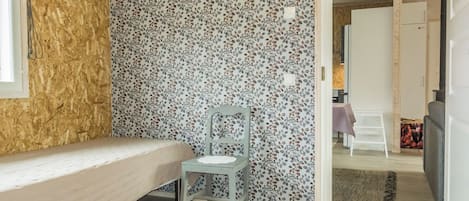 Een slaapkamer met een bed, een stoel, een behang met patroon en een uitzicht op een andere kamer.