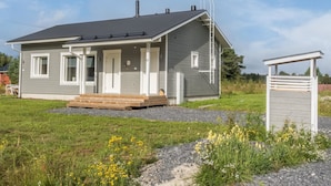 Una casa de un piso con fachada gris, un porche y una pequeña terraza de madera.